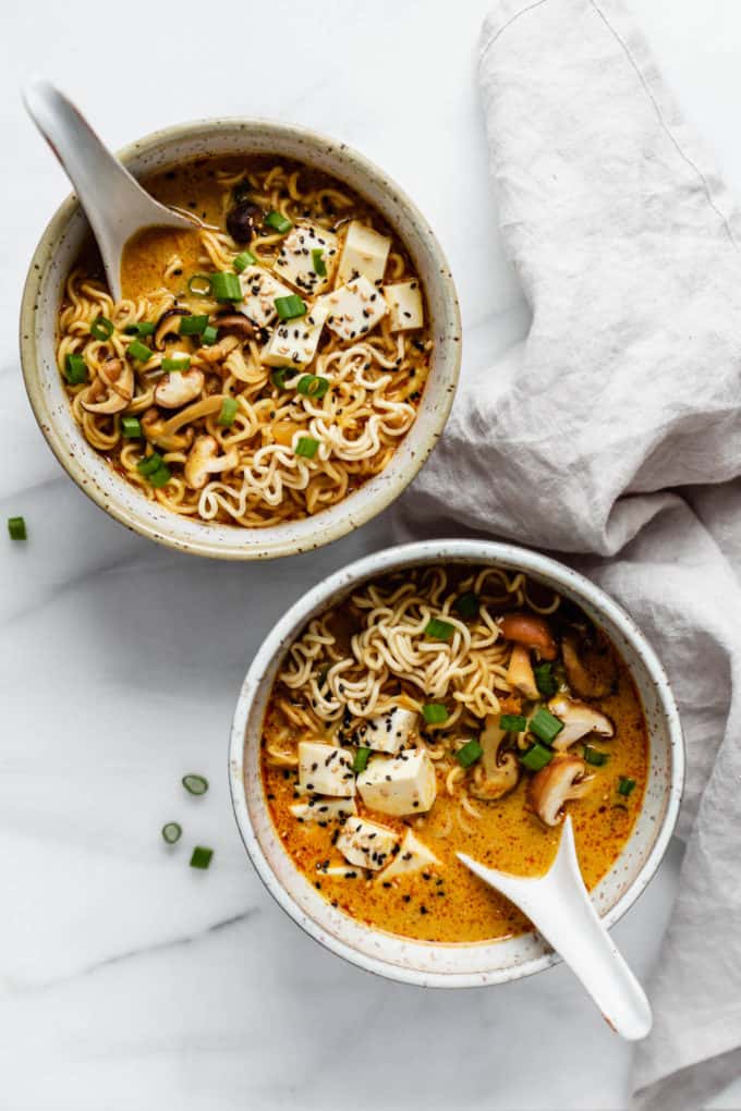two bowls of coconut curry ramen with spoons in them and a napkin on the side