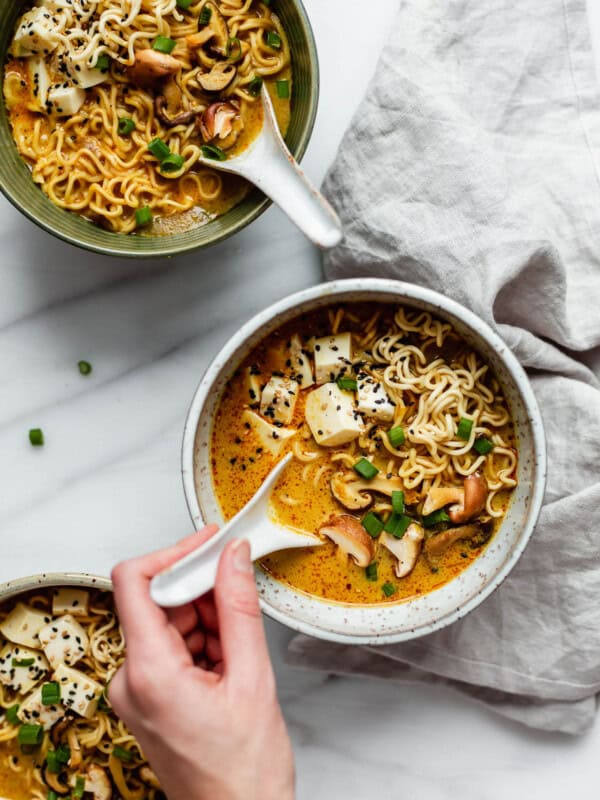 A hand scooping a spoon out of a bowl of coconut curry ramen
