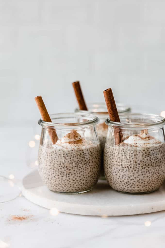 jars of eggnog chia pudding with a cinnamon stick in them