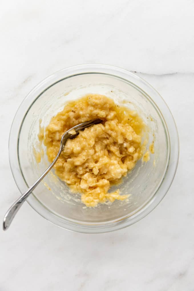 Mashed bananas and a fork in a clear mixing bowl