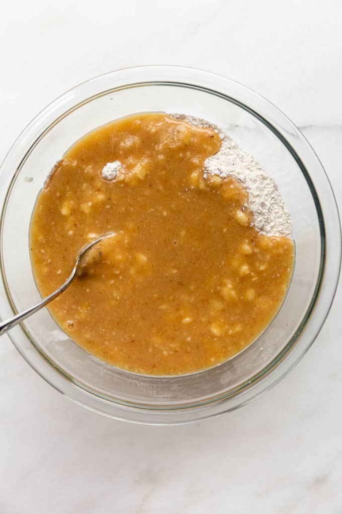 Wet and dry banana bread batter in a clear mixing bowl
