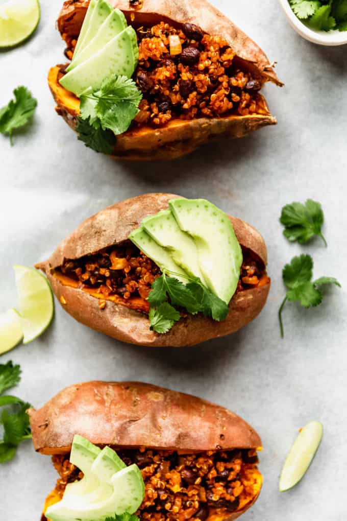 three sweet potatoes stuffed with quinoa and black beans topped with avocado
