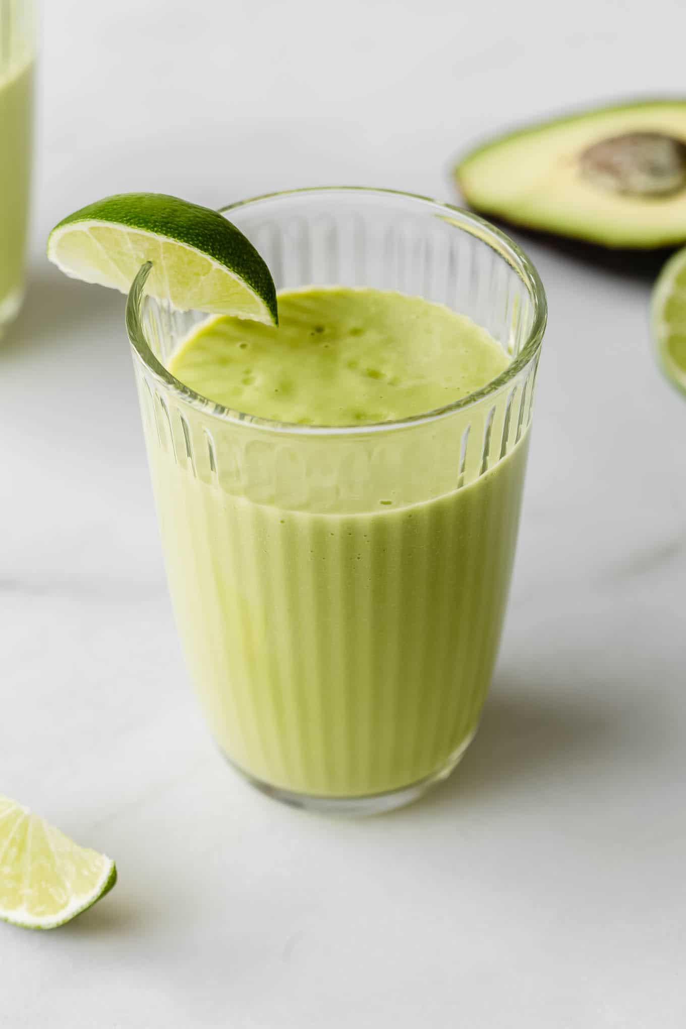 An avocado mango smoothie in a glass with a lime wedge