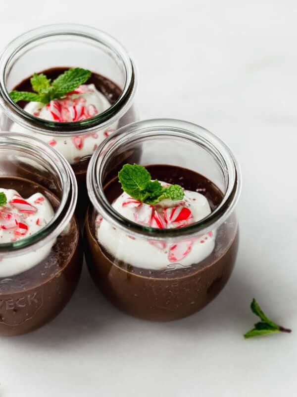 three jars of mint chocolate pudding topped with whipped cream and crushed candy canes