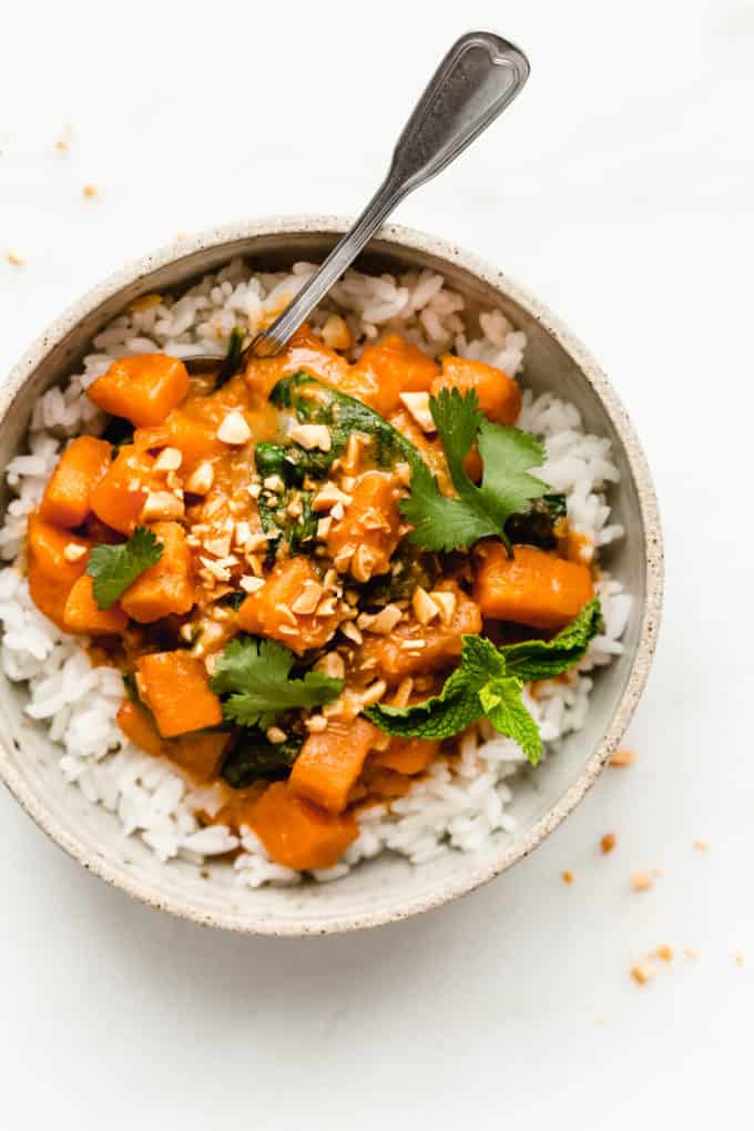 a bowl of sweet potato curry on rice topped with cilantro and mint
