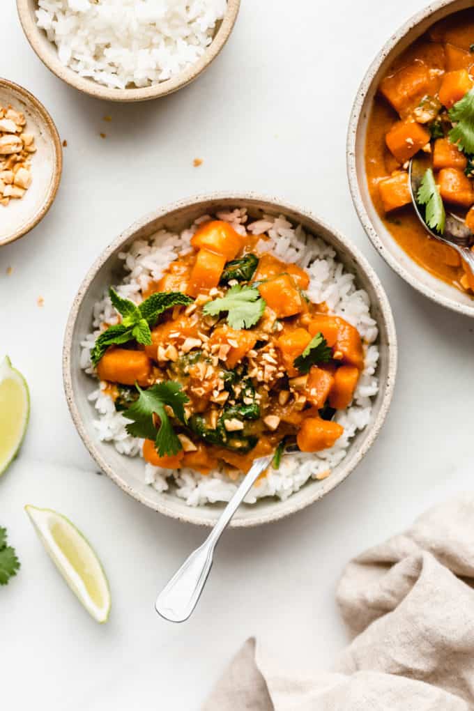 two bowls of sweet potato curry with rice, limes and peanuts on the side
