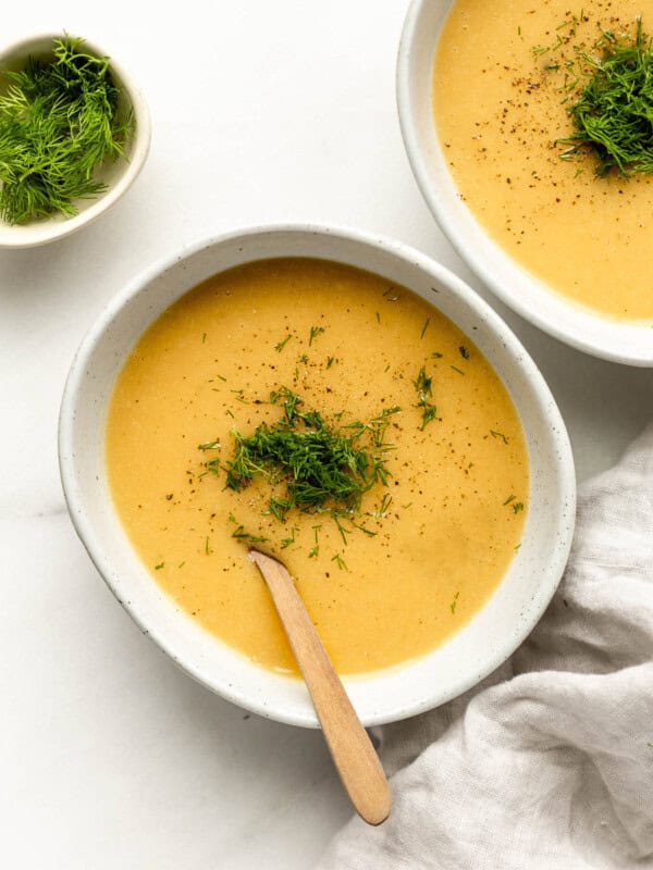 two bowls of vegan potato soup topped with dill with a grey napkin on the side