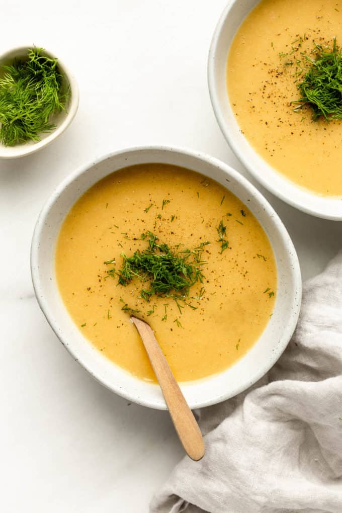 two bowls of vegan potato soup topped with dill with a grey napkin on the side