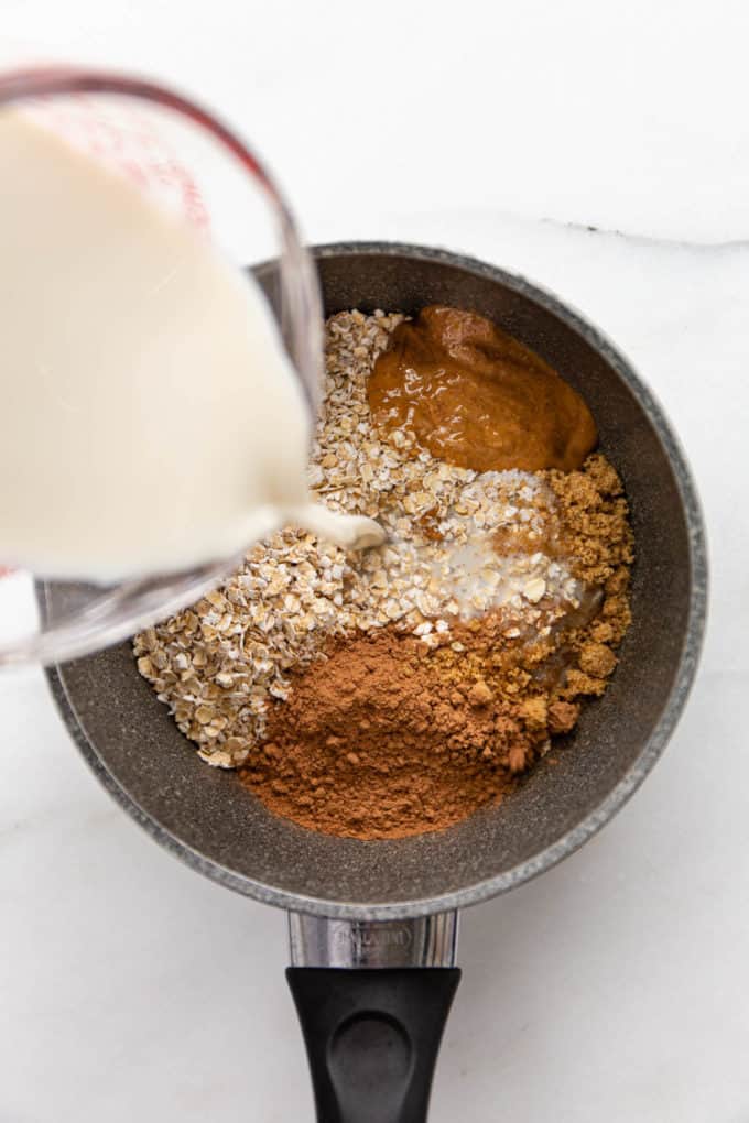 Almond milk being poured into a pot of oats