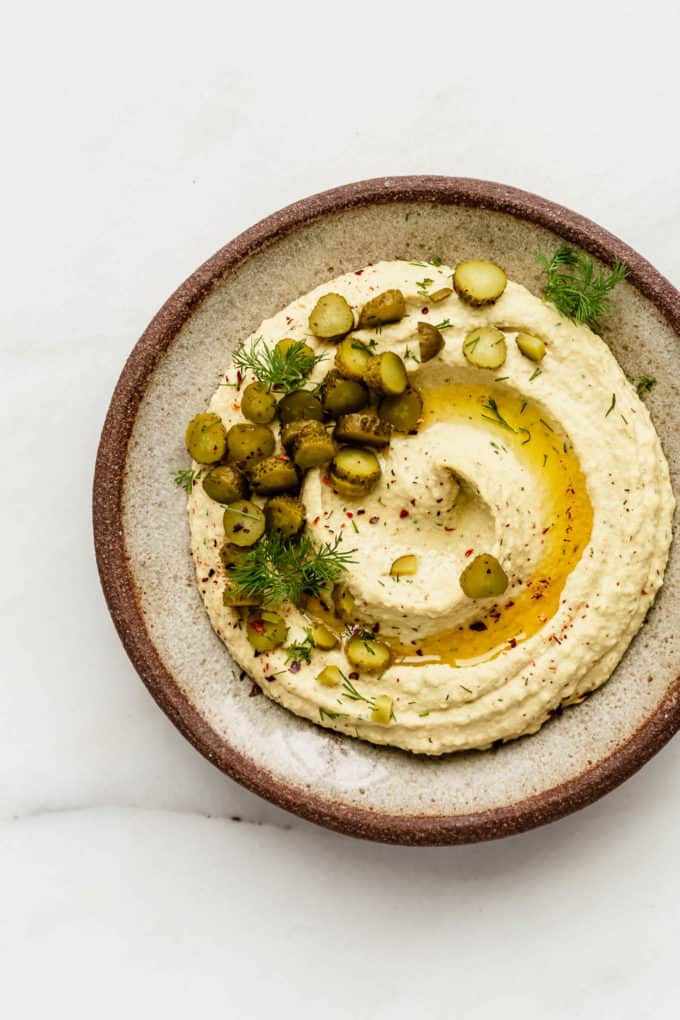 dill pickle hummus in a brown ceramic bowl