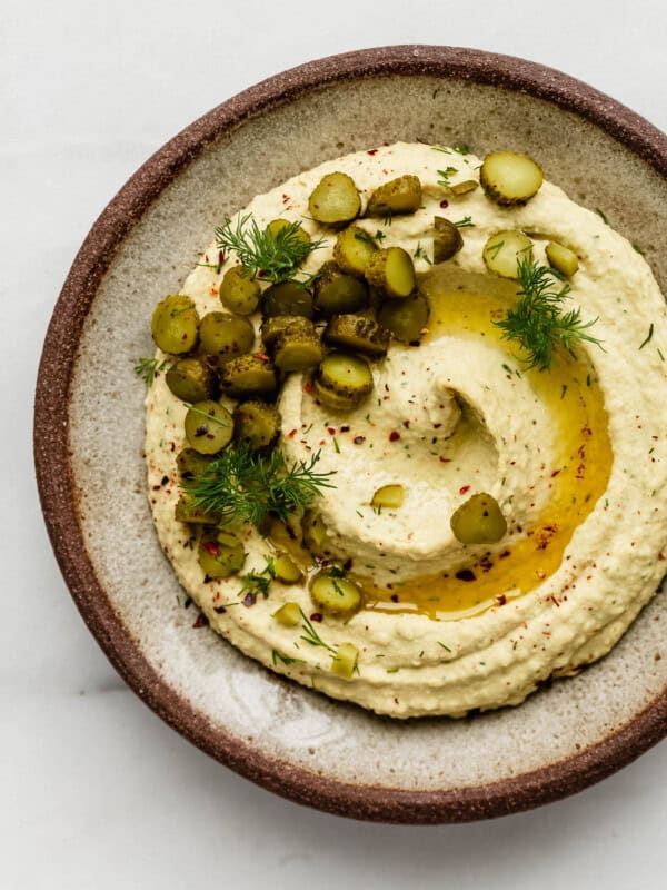 A ceramic plate with dill pickle hummus topped with pickles