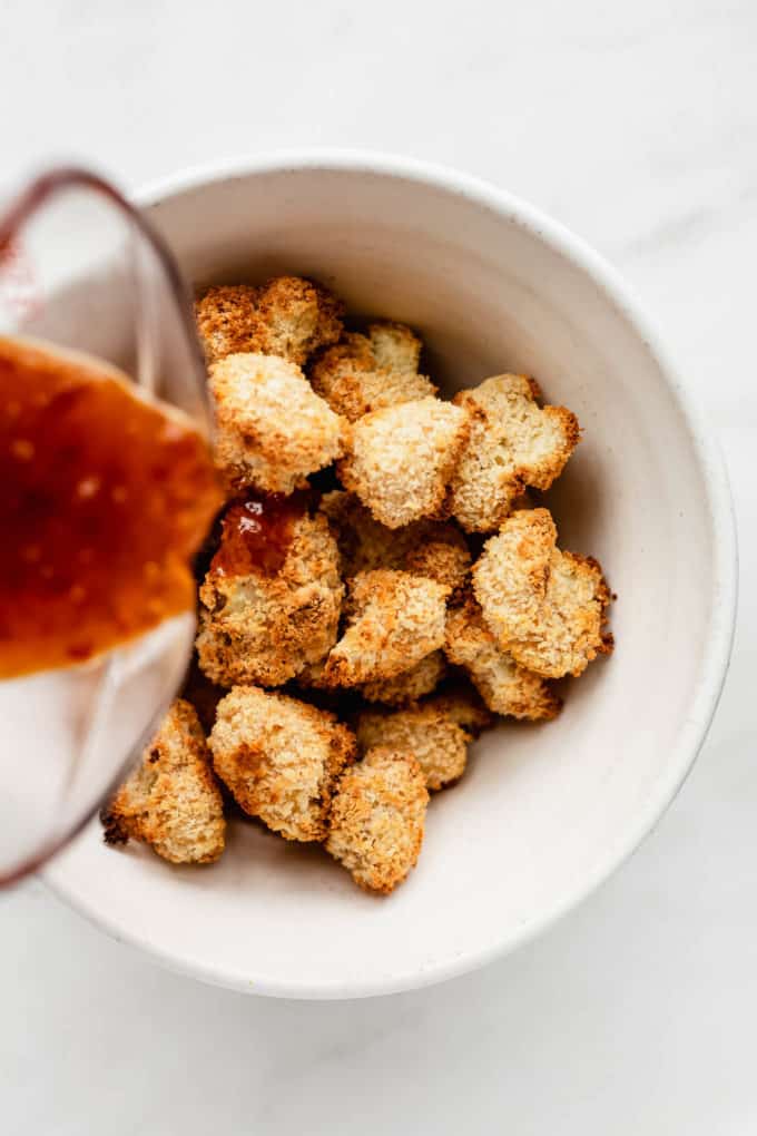 Sauce being poured into a bowl of orange cauliflower