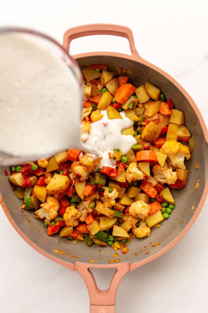 Cashew cream being poured into a pan of vegetables