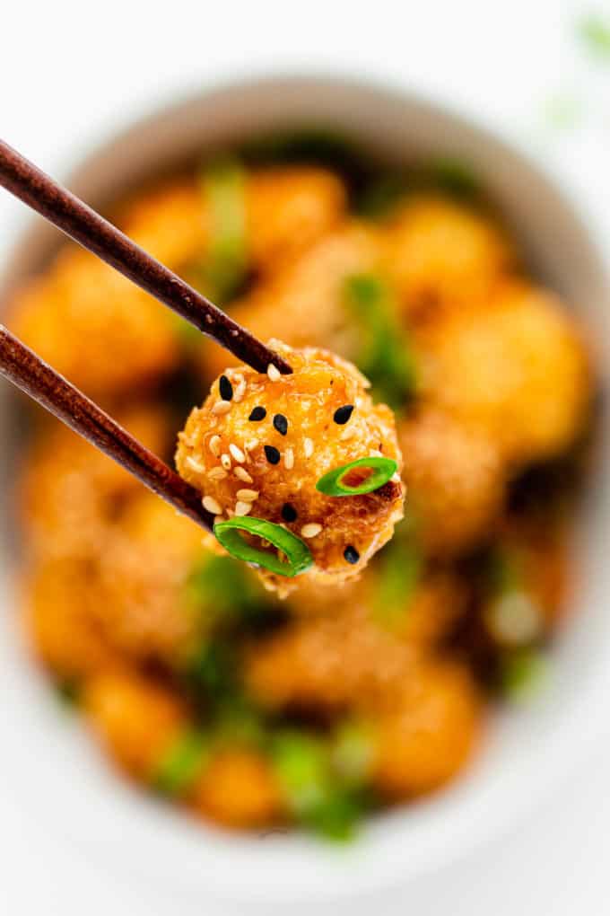 a piece of orange cauliflower being held by chopsticks