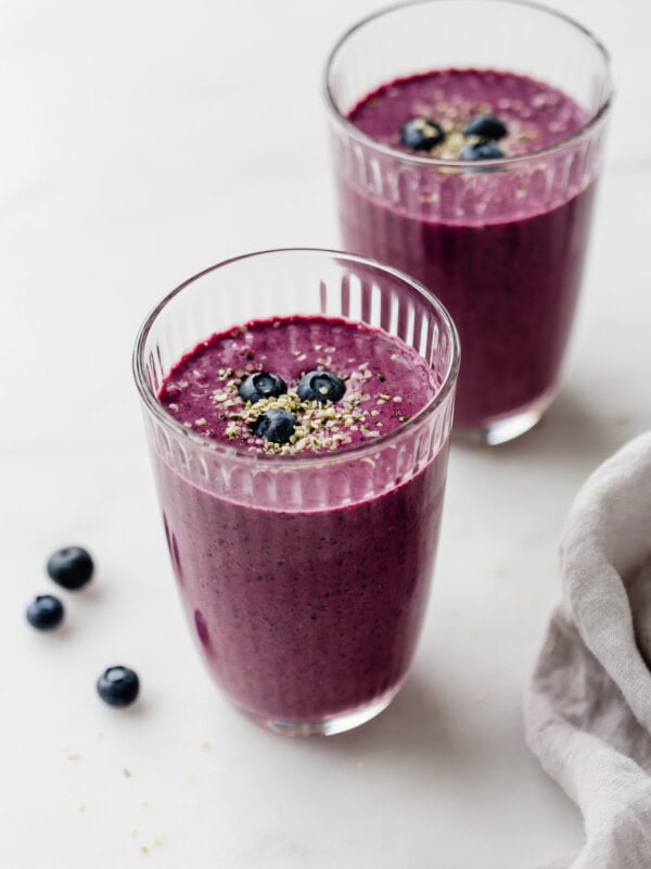 Two glasses of blueberry spinach smoothie topped with hemp seeds and blueberries