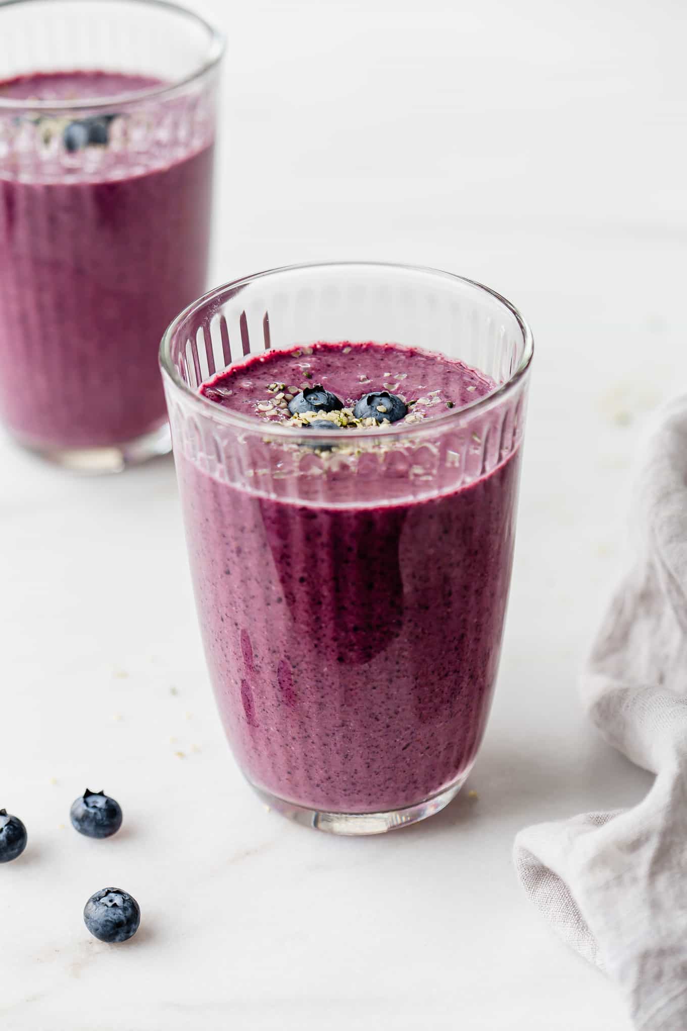 Two glasses of blueberry spinach smoothie with a grey napkin on the side