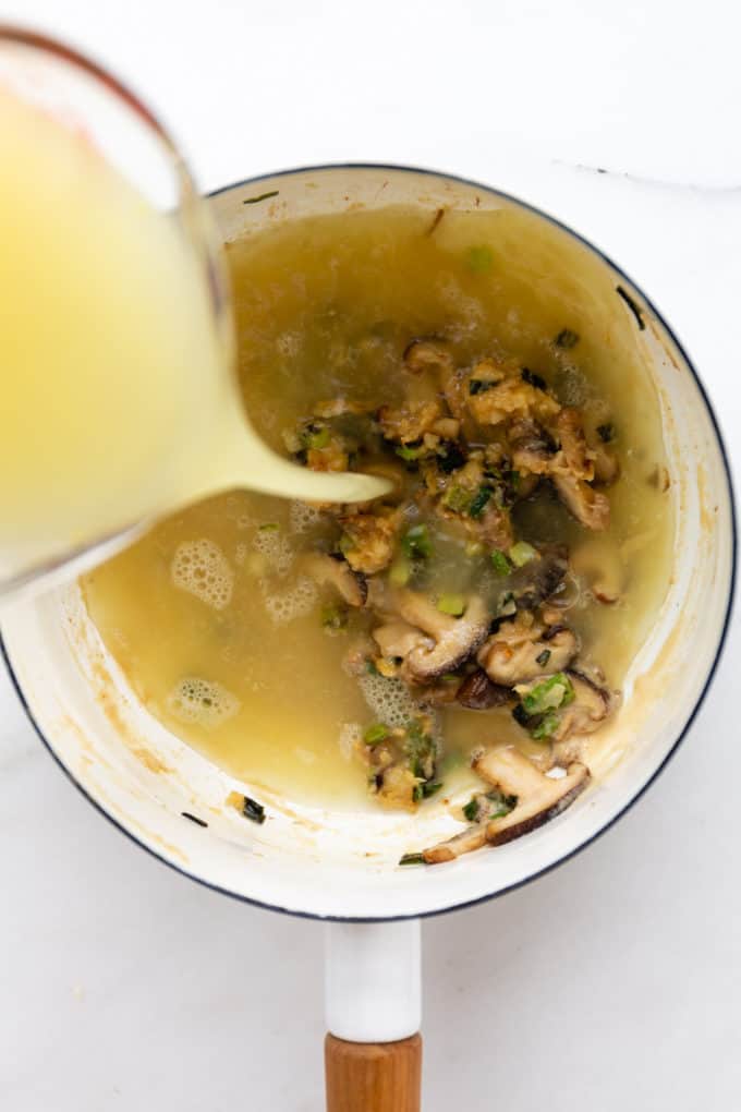 broth being poured into a white pot with shitake mushrooms and miso