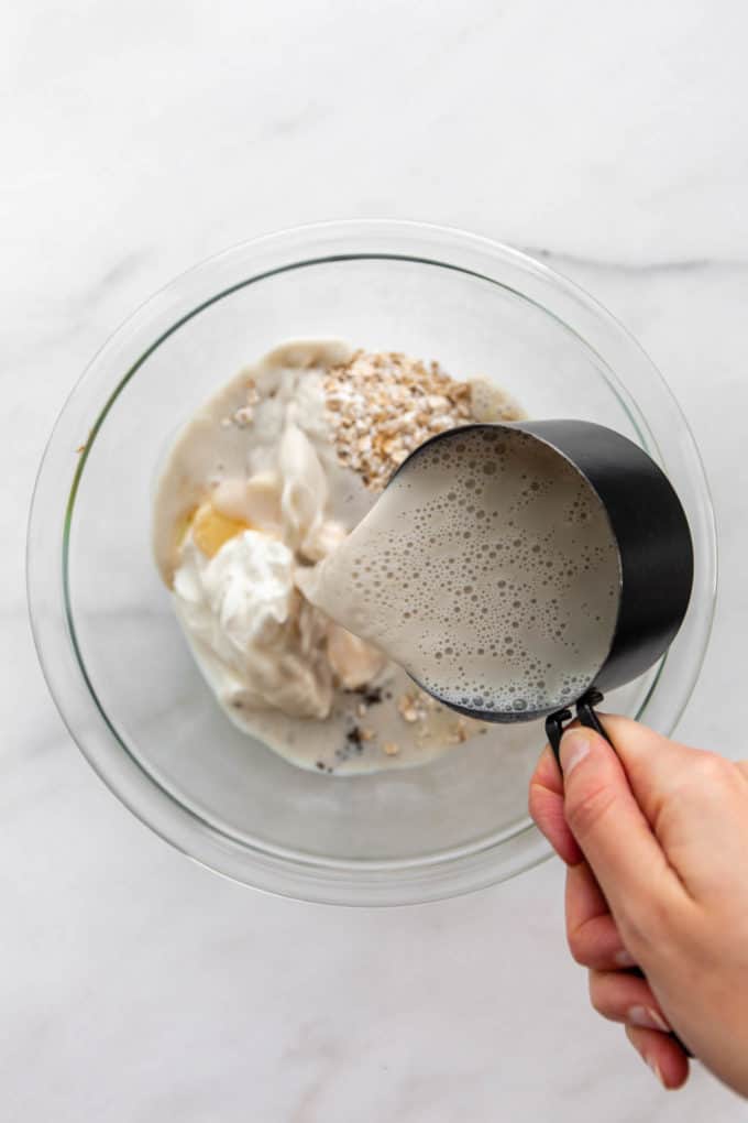 a measuring cup pouring oat milk into a bowl of oats
