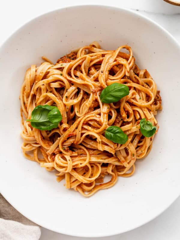 a bowl of red pesto pasta topped with basil leaves