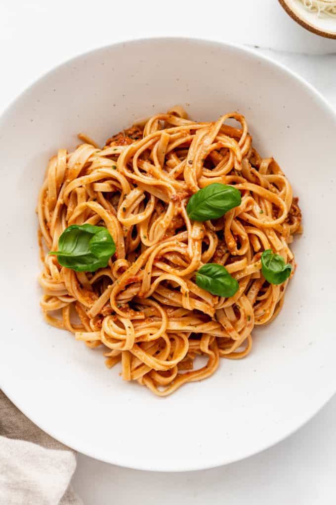 a bowl of red pesto pasta topped with basil leaves