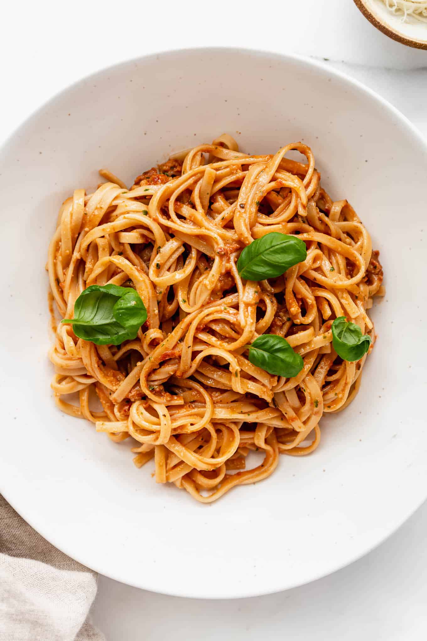 a bowl of red pesto pasta topped with basil leaves