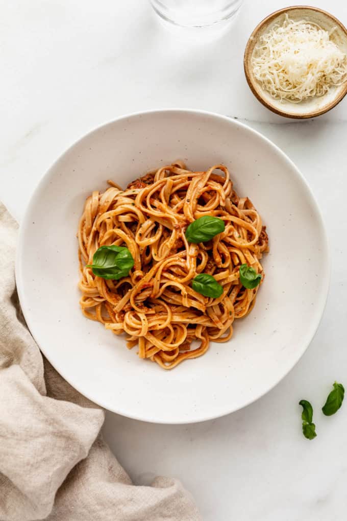 Red pesto pasta in a bowl with a napkin and a small dish of parmesan cheese on the side