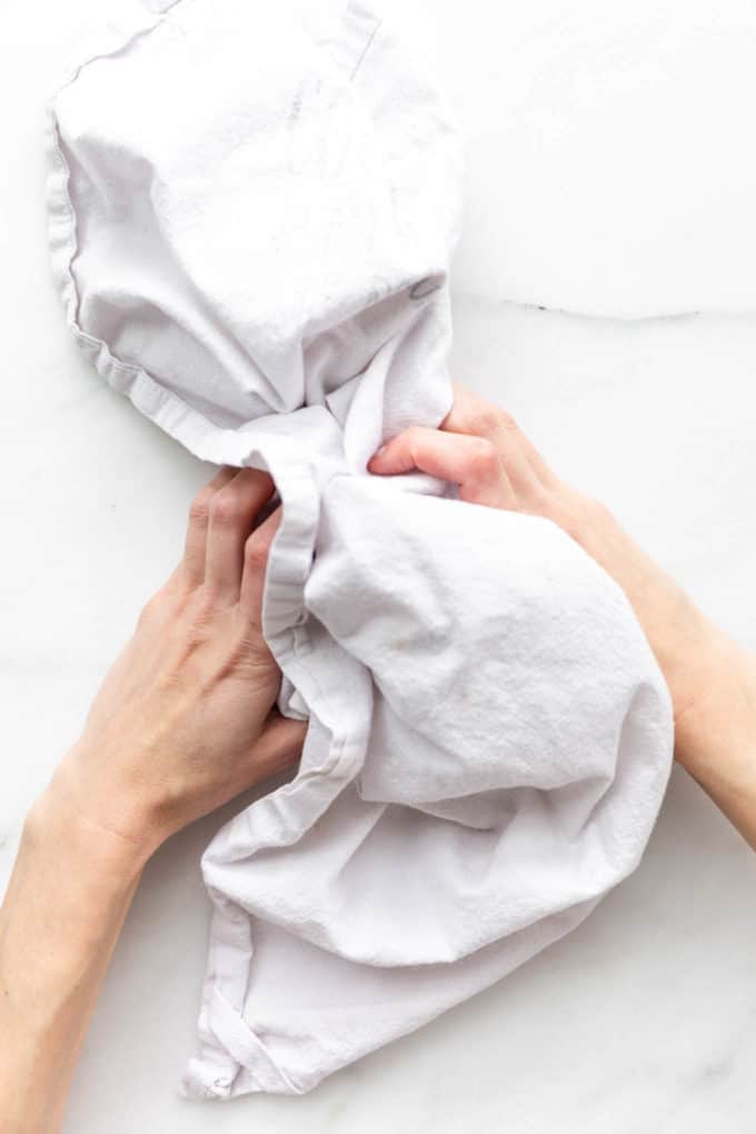 two hands holding a dish towel filled with hazelnuts