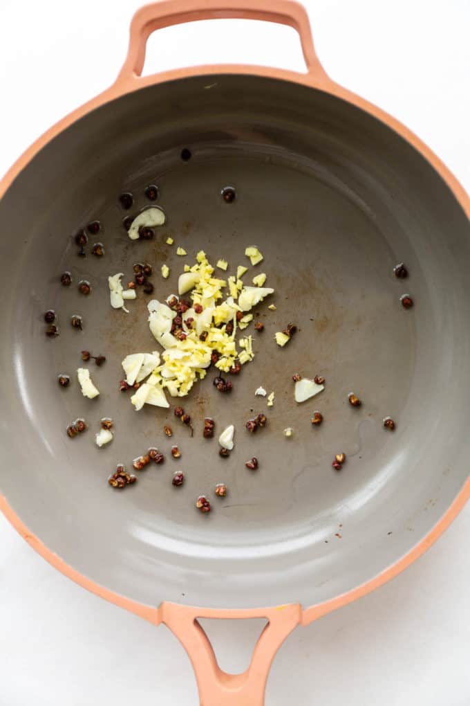 garlic, onions and sichuan peppercorns in a pink pan