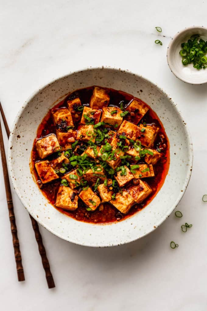 A bowl of mapo tofu with chopsticks and chopped green onions on the side