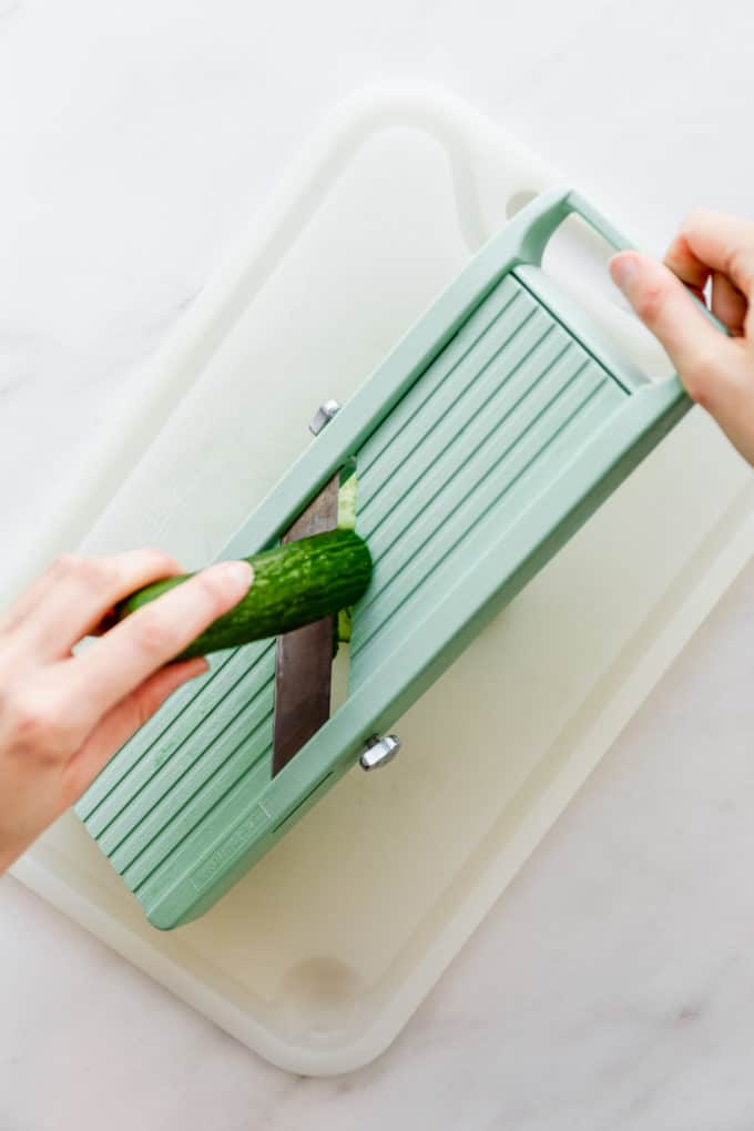 a hand slicing cucumber with a madolin