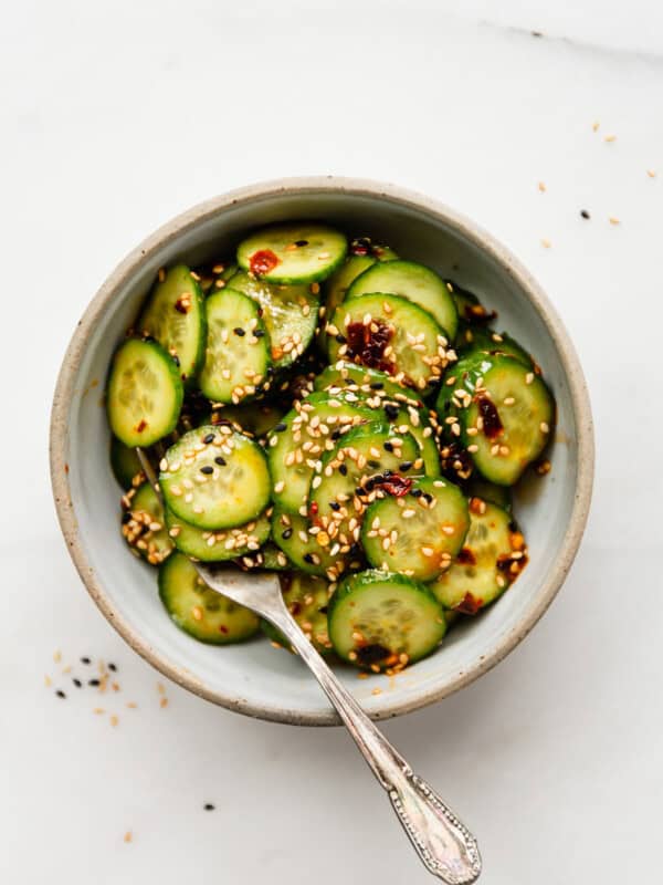 sliced cucumbers in a bowl topped with asian dressing and sesame seeds