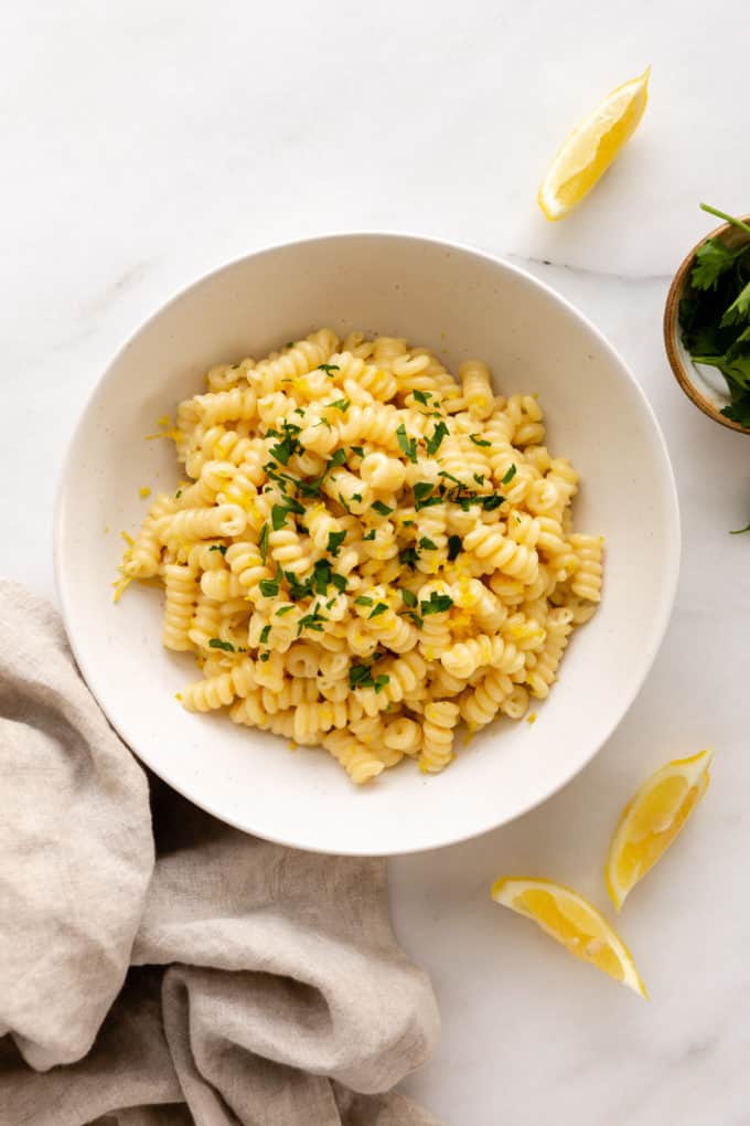 a bowl of lemon pasta with sliced lemons and a napkin on the side