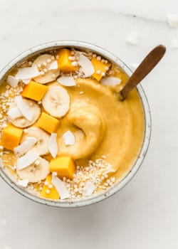A mango smoothie bowl topped with fruits and coconut flakes