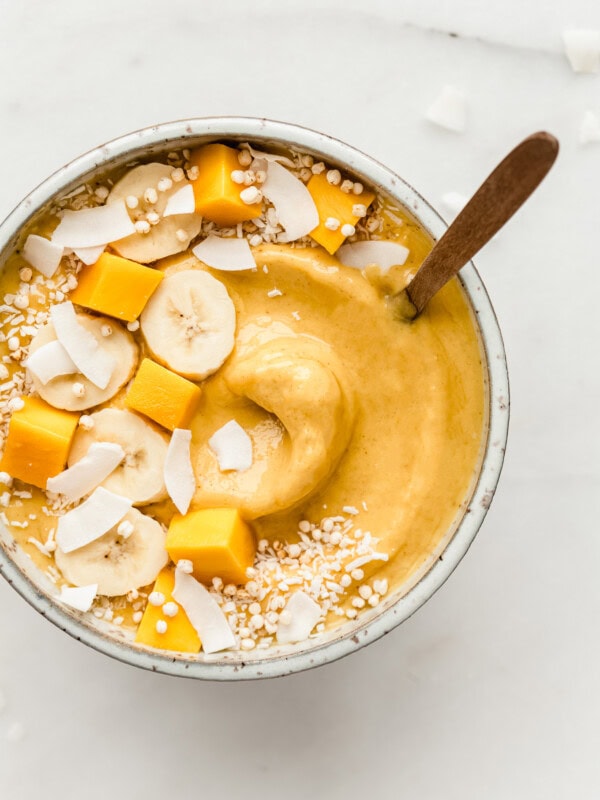 A mango smoothie bowl topped with fruits and coconut flakes