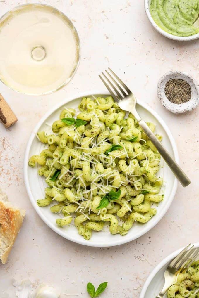 a white plate of avocado pesto pasta topped with basil
