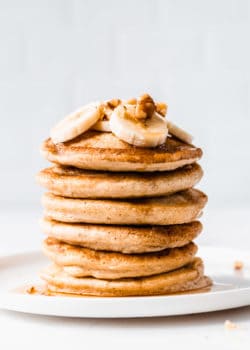 a stack of 6 oat flour pancakes with bananas and walnuts on top