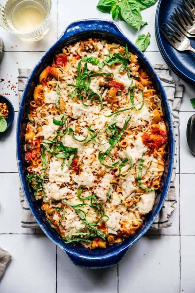 a blue baking dish of vegan pasta topped with basil