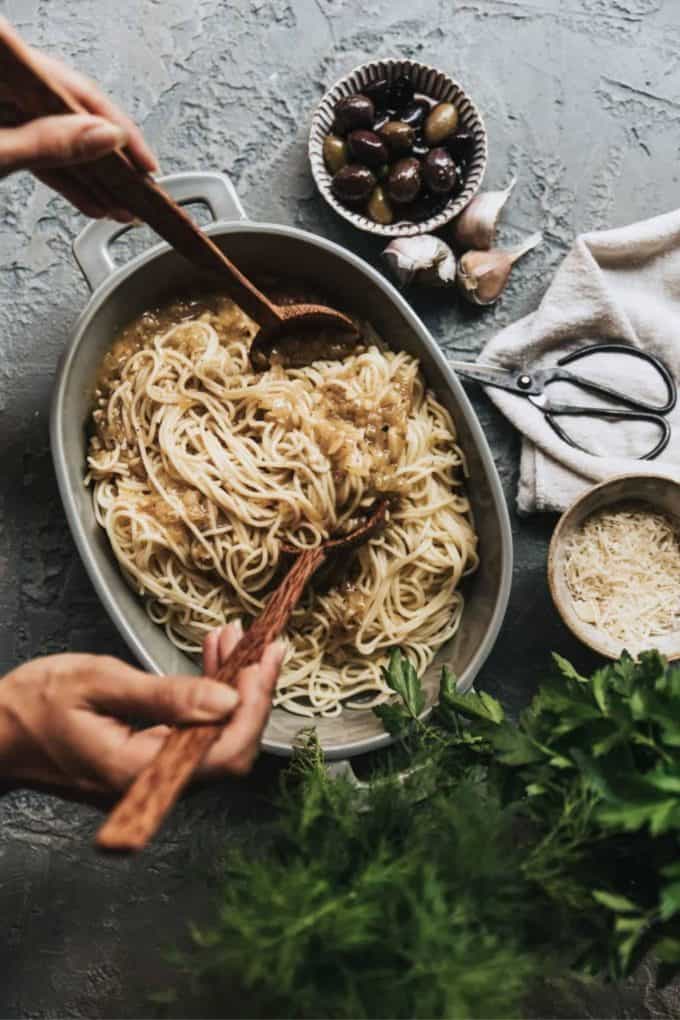 spaghetti in a grey baking dish with olives and garlic on the side