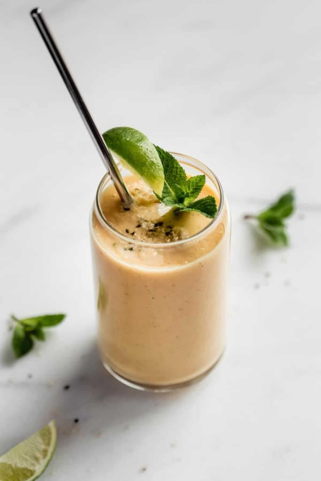 A yellow smoothie topped with a sprig of mint and a lime wedge