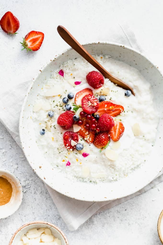 a bowl of coconut rice pudding topped with berries with a wood spoon in it