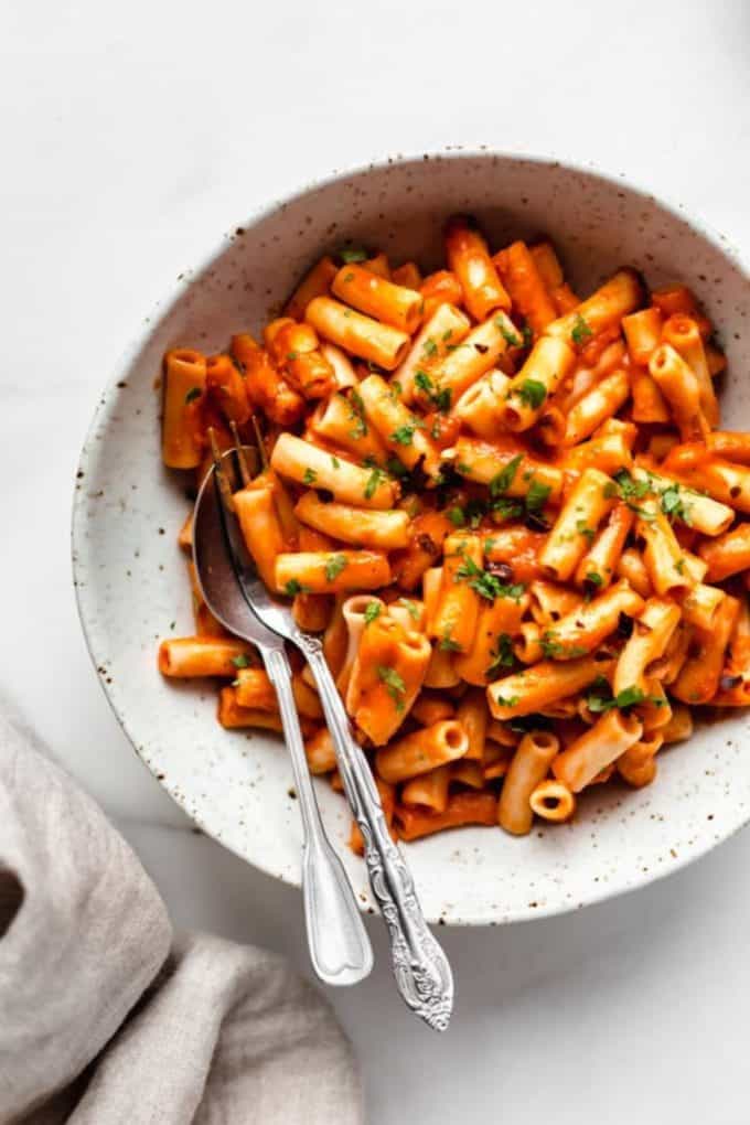 roasted red pepper pasta in a white speckled bowl with a fork and spoon in it