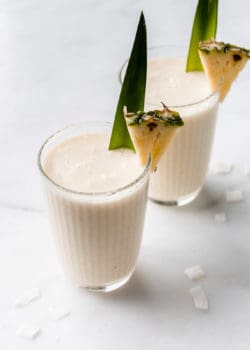 two glases of pina colada smoothies wit a pineapple in them