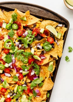 nachos topped with avocado, salsa and cilantro on a baking sheet
