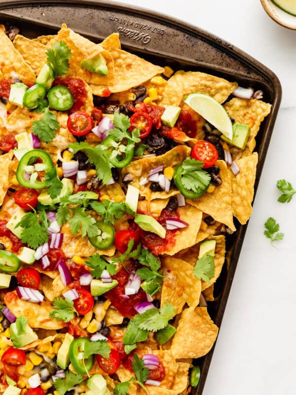 nachos topped with avocado, salsa and cilantro on a baking sheet
