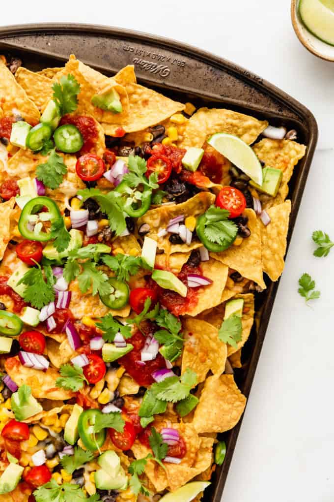 nachos topped with avocado, salsa and cilantro on a baking sheet