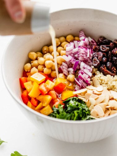 dressing being poured into a bowl of quinoa chickpea salad