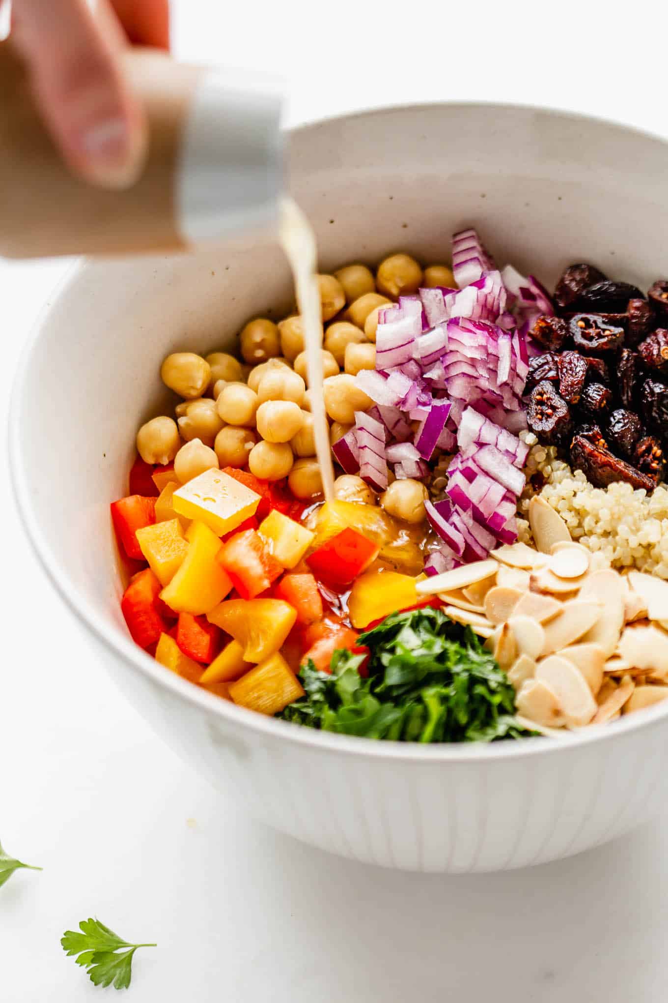 dressing being poured into a bowl of quinoa chickpea salad