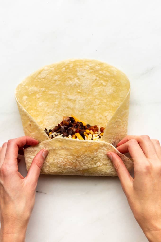 a tortilla with stuffing half rolled into a burrito