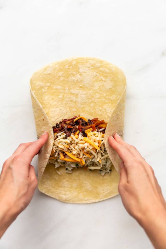 a hand rolling a veggie burrito