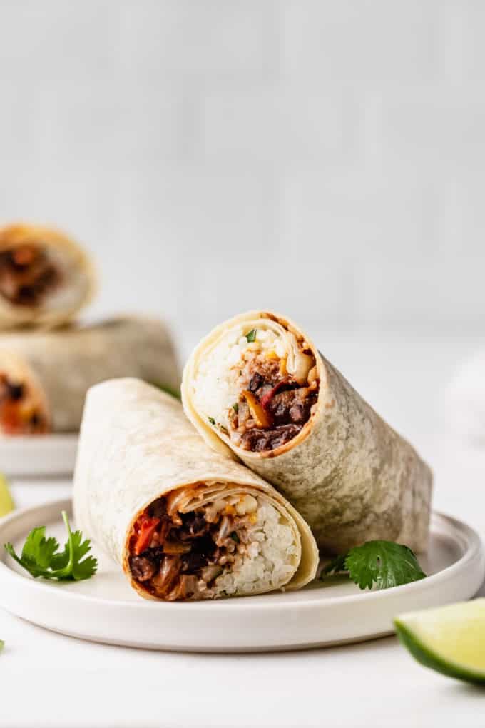 a veggie burrito on a white plate with cilantro